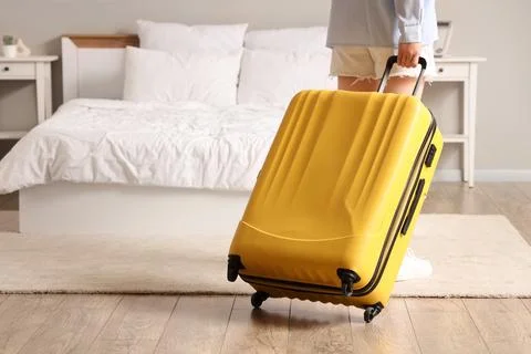 Person pulling a yellow suitcase on wheels in a bedroom, travel and vacation  Stock Photos