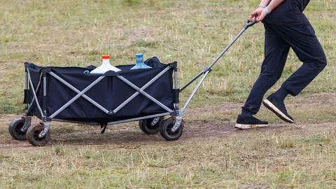 Person pulls black foldable wagon across grassy field Stock Photos