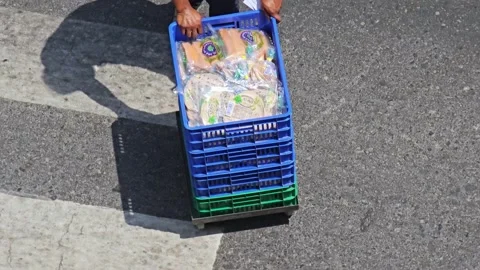A person pulls a blue cart filled with Al Arz Arabic bread across a sunlit Stock Footage 311885791