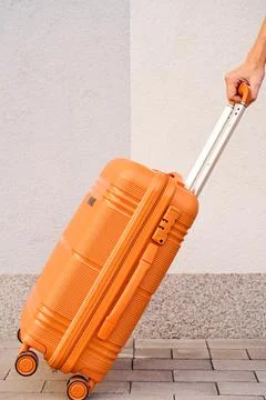 Person pulls an orange rolling suitcase along a paved walkway beside a ligh.. Stock Photos