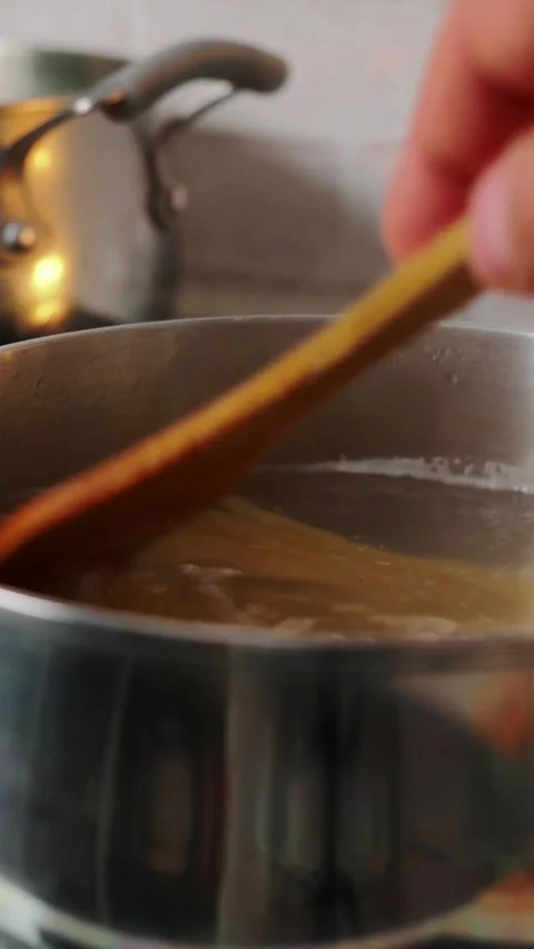 Person pushing dry spaghetti into stainless pot filled with simmering hot water Stock Footage 346641073