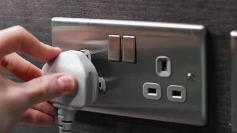 Person puts a UK plug into a three holed socket and turns it on by the Stock Footage 143392914