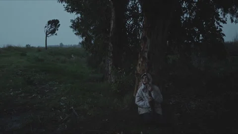 Person in raincoat sheltering from storm under a tree Stock Footage 330564778