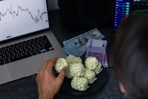 Person reaching for dessert while working on a laptop with financial charts.. Foto stock