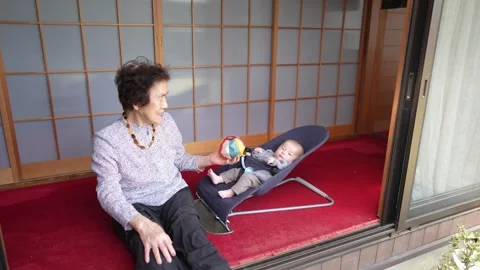 Person Reaching Patterned Ball Toward Baby in Bouncer Stockbeeldmateriaal 344858380