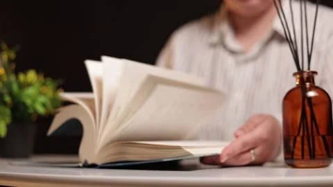 Person reading a book with an aroma diffuser and plant in soft lighting Stockbeeldmateriaal 339212044