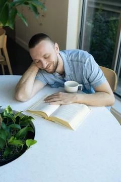 Person reading book while working remotely at a table with a plant holding .. Fotos Stock