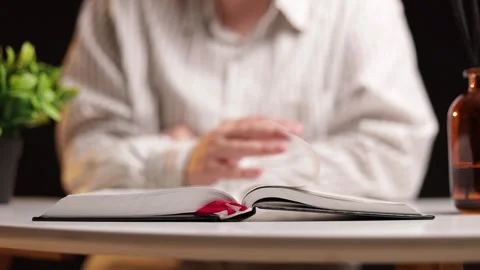 Person reading an open book with a red bookmark on a table Stock Footage 339215541