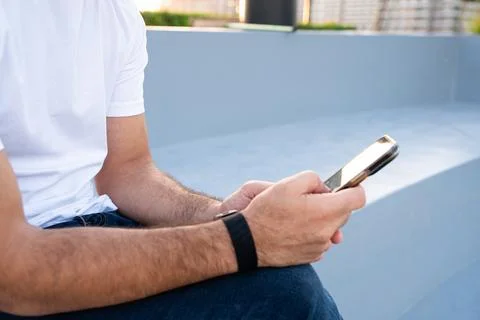 Person reading smartphone while sitting on modern outdoor bench in bright Stock Photos