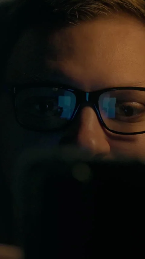 A person reading on a smartphone while wearing glasses in a dimly lit room d Stock Footage 331530637