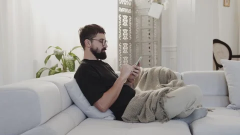 A person reclining on a couch while using a cell Stock Footage 265403949