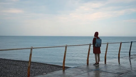 Person in red jacket lonely stands on pier in rain on sea shore Stock Footage 118448575