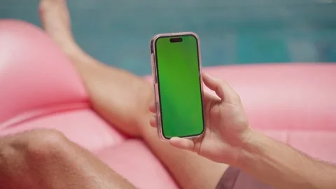 Person Relaxing on Pink Pool Float With Green Screen Smartphone in Hand Stock Footage 267785766