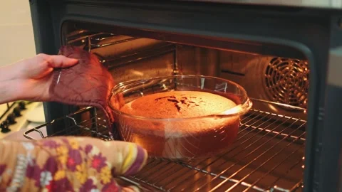 Person removing baked dish from kitchen oven with floral oven mitts Vidéo 342885188
