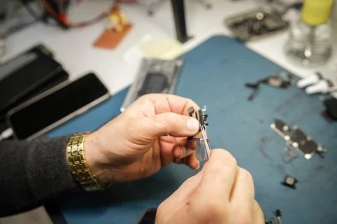 Person Repairs Small Electronic Device at Workbench During Daytime in a Workshop Stock Photos