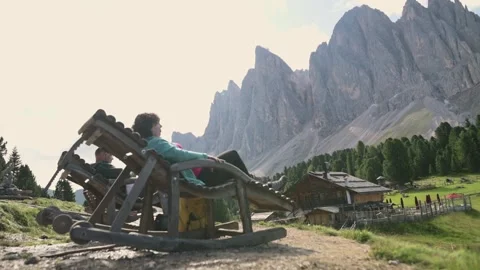 Person resting in large rustic chair in front of Dolomites mountain range, Italy Stock Footage 319670545