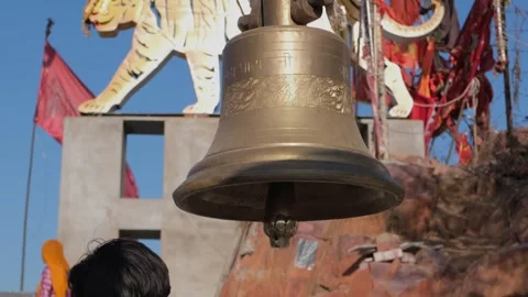 Person ringing a large brass bell at a Hindu temple Видео 329854869