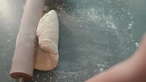 A person rolls out dough on a flat surface using a rolling pin in a kitchen. The Stock Footage 339094410