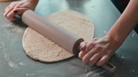 A person rolls out dough on a flat surface using a rolling pin. The kitchen is Video stock 339094427
