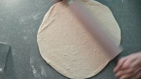 A person rolls out dough using a rolling pin on a countertop in a kitchen Stock Footage 339094428