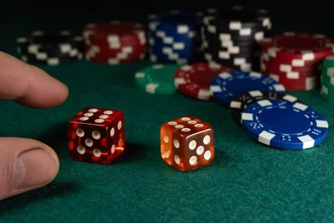 A person rolls two dice while surrounded by various poker chips on a green .. Stockfoto's
