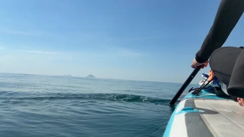 Person rowing a paddleboard on calm open sea with distant islands under a clear 스톡 동영상 341408888