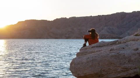 Person sat down with a VR head set on looking over a lake at sunset Stock Photos