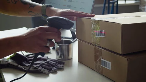 Person Scanning Barcode on Cardboard Box at Warehouse Desk 動画素材 337306525