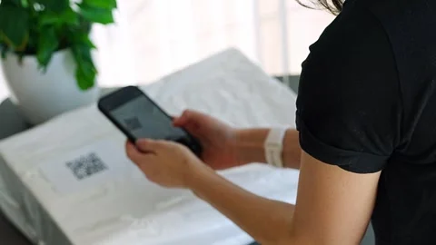 Person scanning QR code on parcel with smartphone camera for delivery tracking Stock Footage 345657550