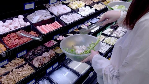  A person scoops assorted hot pot ingredients into a bowl at a self-serve buffet Video stock 323277671