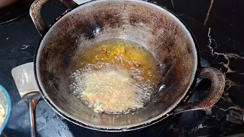 A person scoops vegetable batter into a traditional wok filled with hot oil.. 库存影片 341867932