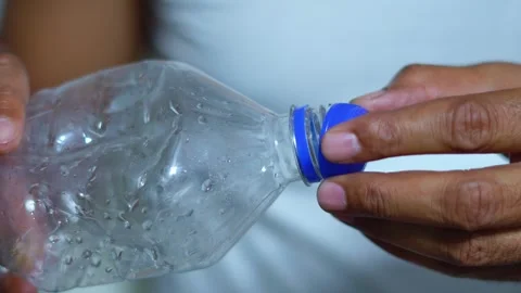 Person screwing the blue cap back on a used plastic water bottle for recycling Stock Footage 345189072
