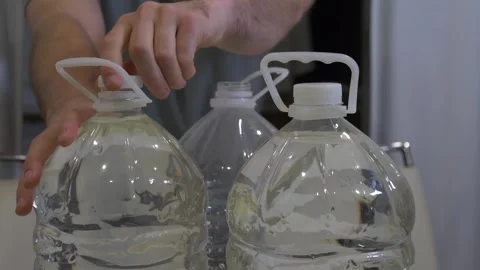 A person is screwing caps onto plastic drinking water bottles on kitchen table Stock Footage 340209136