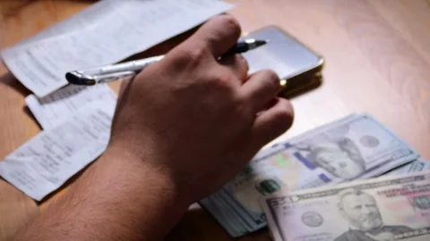 The person is scribbling notes next to a calculator and money Stock Footage 264983046