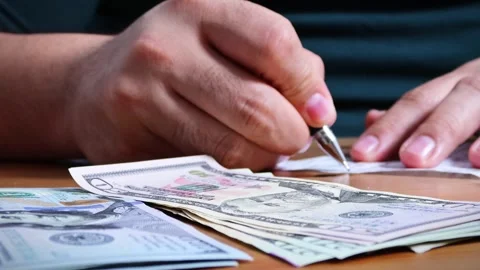 The person is scribbling notes next to a calculator and money Stock Footage 264983056