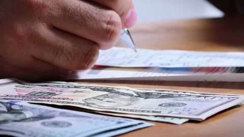 The person is scribbling notes next to a calculator and money Stock Footage 264983105