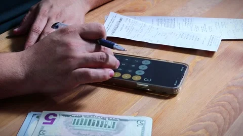 The person is scribbling notes next to a calculator and money Stock Footage 264983195
