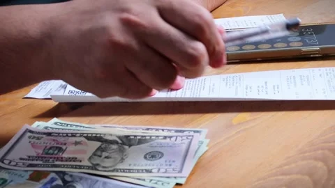 The person is scribbling notes next to a calculator and money Stock Footage 264983426