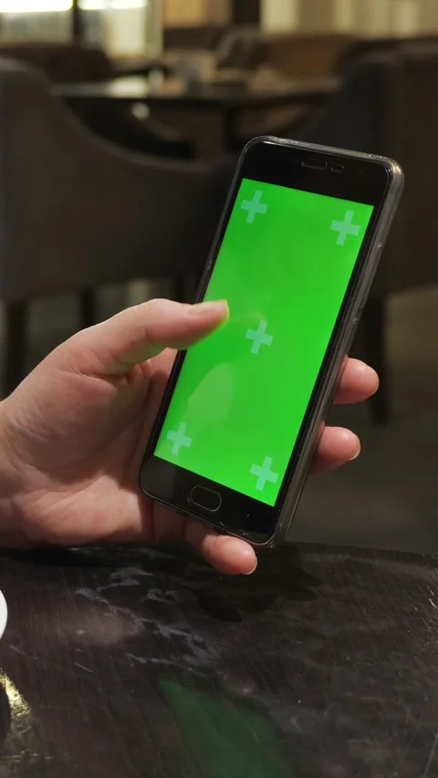 Person scrolling a smartphone with a green screen in a cafe. Closeup of a hand Stock Footage 341580111