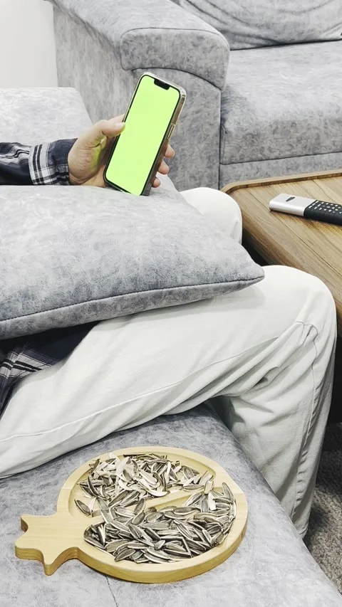 Person scrolling on smartphone while eating sunflower seeds, vertical Stock Footage 345153959