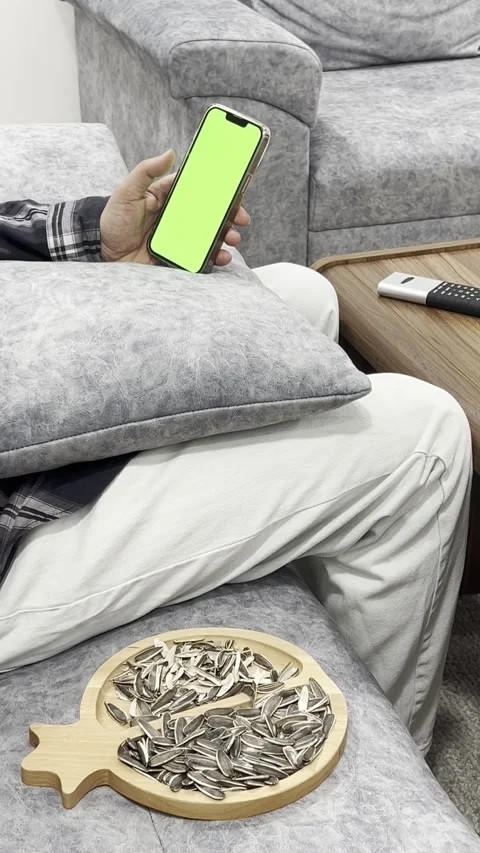 Person scrolling on smartphone while eating sunflower seeds, vertical Stock Footage 345154193