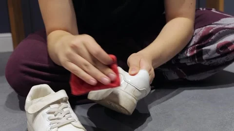 Person scrubbing sneaker side on gray floor 스톡 동영상 337955373