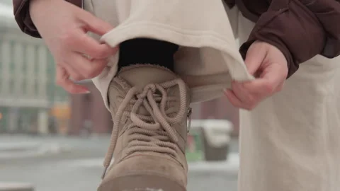 Person securing pant cuff over snow-dusted winter boot while adjusting laces 動画素材 347614138