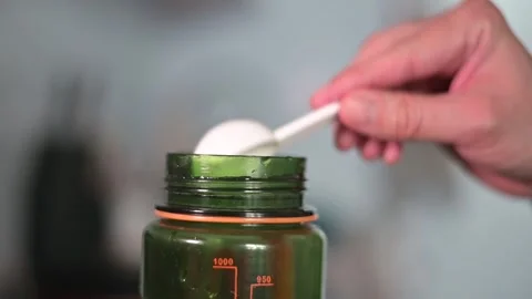 A person is seen adding a powder into a clear bottle in a kitchen setting. The Video stock 338188278