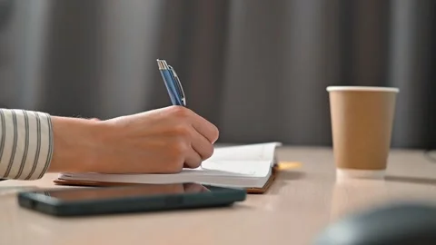 A person is seen turning a page in a notebook and writing notes at a table. The Stock Footage 339005750