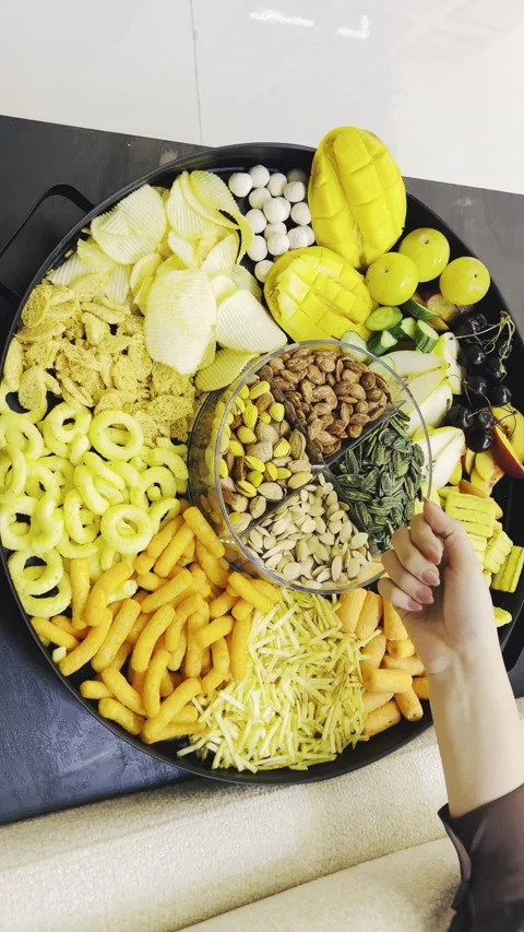 Person selecting snacks and nuts from a large tray on a desk Stock Footage 345146216