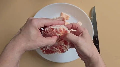 A person separating a grapefruit into segments by hand over a white plate Stock Footage 342027736