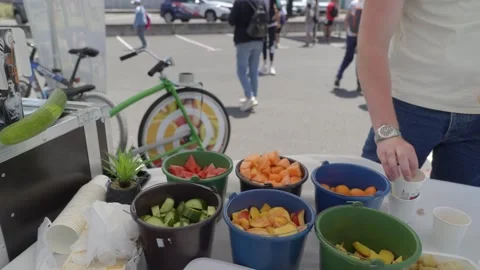 Person Serving Fresh Fruit at Outdoor Event in Toulouse with Bicycles and Crowd Stock Footage 347124329