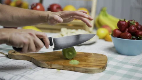 Person with sharp knife cutting slices of kiwi near other fruit in kitchen - Stock Footage 341026716