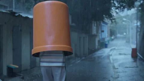 Person sheltering from heavy rain under a bucket on the street Stock Footage 333804416